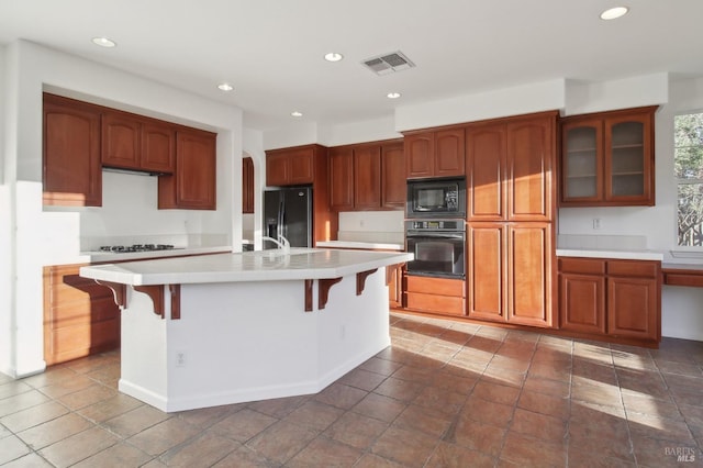 kitchen with a kitchen breakfast bar, a center island with sink, and black appliances