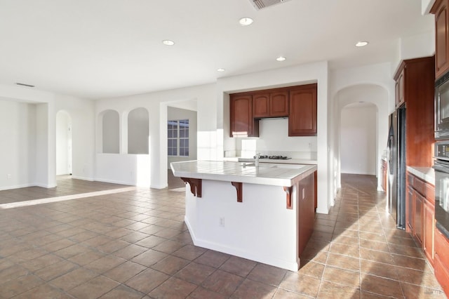 kitchen featuring a kitchen breakfast bar, built in microwave, tile counters, black oven, and fridge