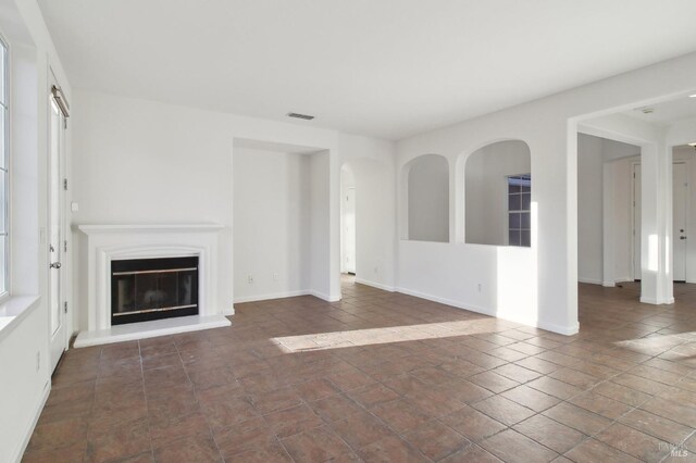 spare room featuring arched walkways, baseboards, visible vents, and light colored carpet