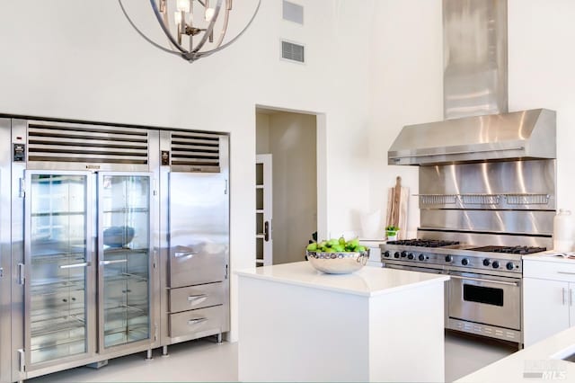 kitchen with decorative light fixtures, light countertops, white cabinets, wall chimney range hood, and double oven range