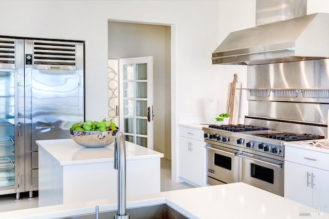 kitchen with wall chimney exhaust hood, premium appliances, light countertops, and white cabinetry