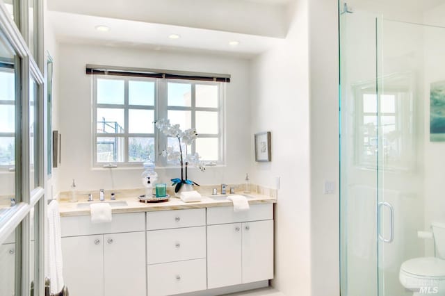 full bath with toilet, a stall shower, double vanity, and a sink