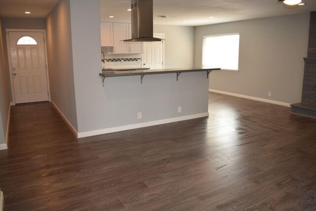 kitchen featuring decorative backsplash, kitchen peninsula, a breakfast bar, ventilation hood, and white cabinetry