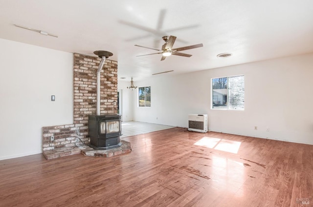 unfurnished living room with a wood stove, plenty of natural light, visible vents, and wood finished floors