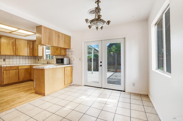 kitchen featuring light tile patterned floors, a peninsula, french doors, tile counters, and decorative backsplash