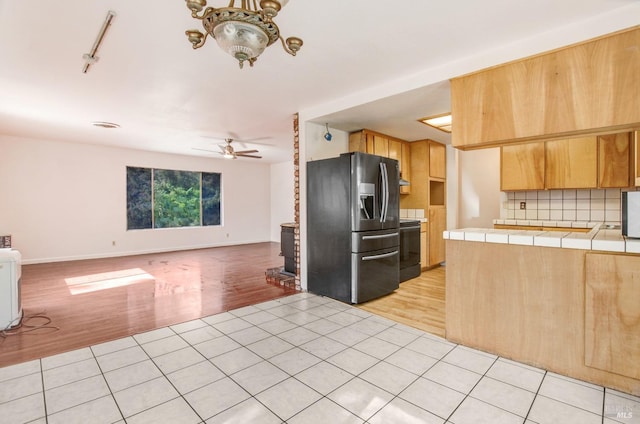 kitchen with light tile patterned floors, tasteful backsplash, stainless steel fridge, tile counters, and open floor plan