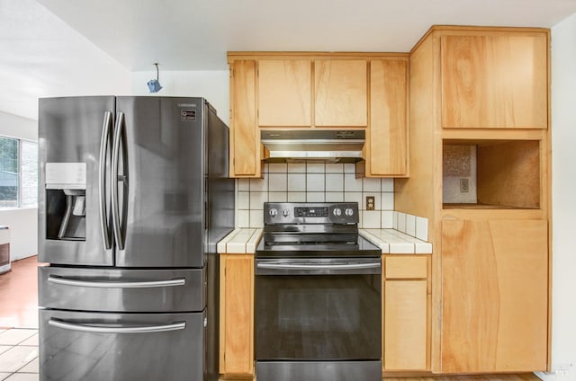 kitchen with under cabinet range hood, electric range, tile counters, and stainless steel refrigerator with ice dispenser