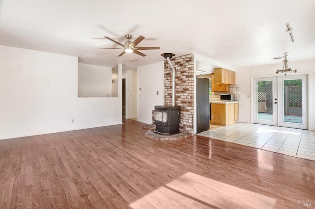 unfurnished living room featuring a ceiling fan, baseboards, light wood-style floors, french doors, and a wood stove