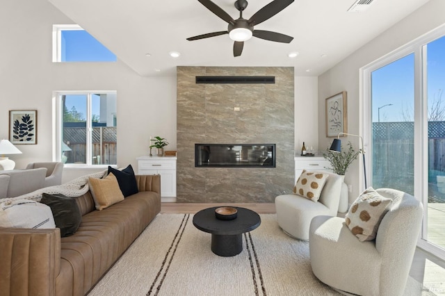 living room with ceiling fan, a tiled fireplace, and light wood-type flooring