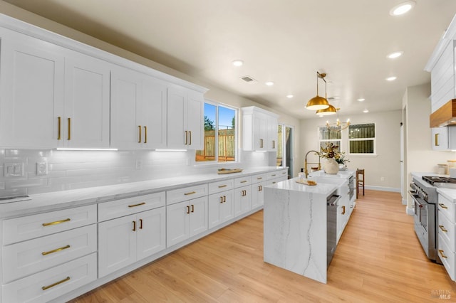 kitchen with white cabinetry, hanging light fixtures, an island with sink, and appliances with stainless steel finishes