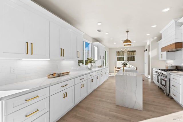 kitchen with white cabinetry, double oven range, decorative light fixtures, and light stone countertops