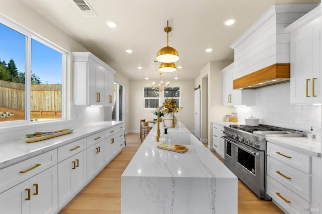 kitchen featuring hanging light fixtures, light stone countertops, white cabinets, a kitchen island, and range with two ovens