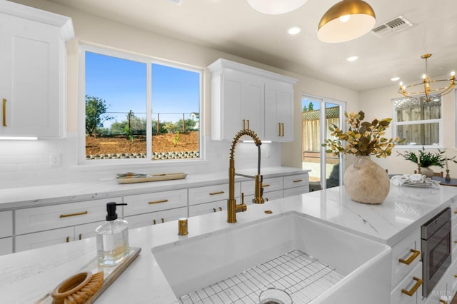 kitchen featuring sink, stainless steel microwave, plenty of natural light, pendant lighting, and white cabinets