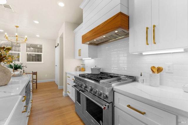 kitchen featuring double oven range, hanging light fixtures, light stone counters, white cabinets, and a barn door