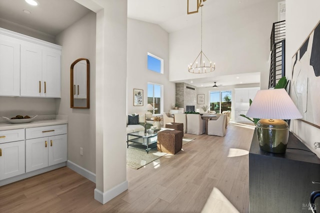 interior space featuring ceiling fan with notable chandelier, light hardwood / wood-style floors, and a towering ceiling