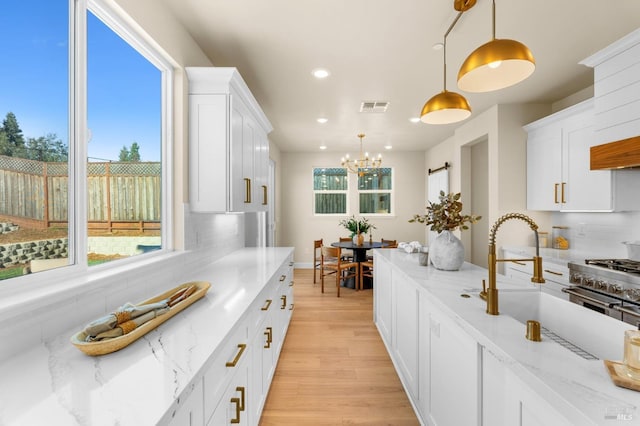 kitchen with tasteful backsplash, light stone countertops, pendant lighting, and white cabinets