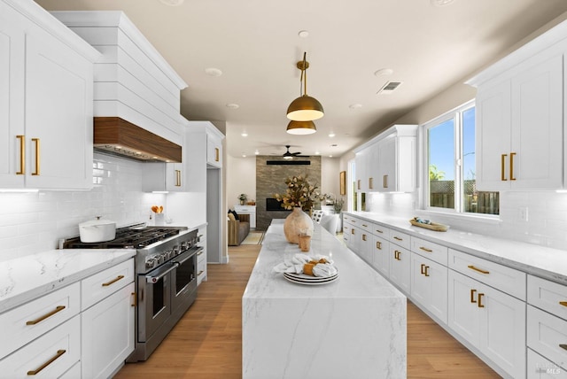 kitchen with light stone counters, white cabinetry, double oven range, and hanging light fixtures