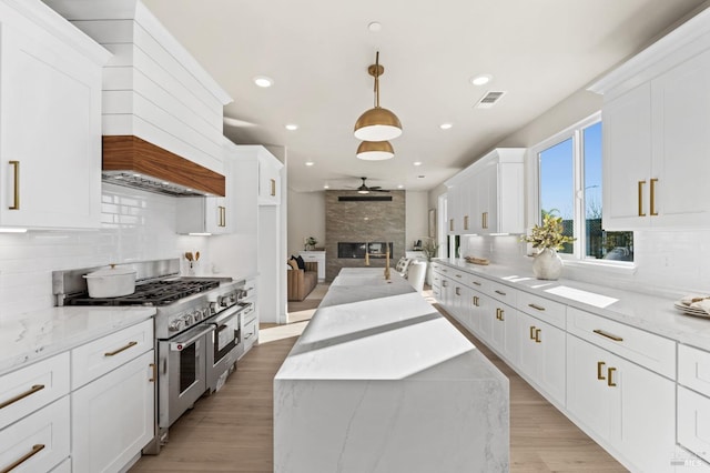 kitchen featuring range with two ovens, hanging light fixtures, and light stone counters