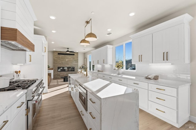 kitchen featuring hanging light fixtures, an island with sink, white cabinetry, and ceiling fan