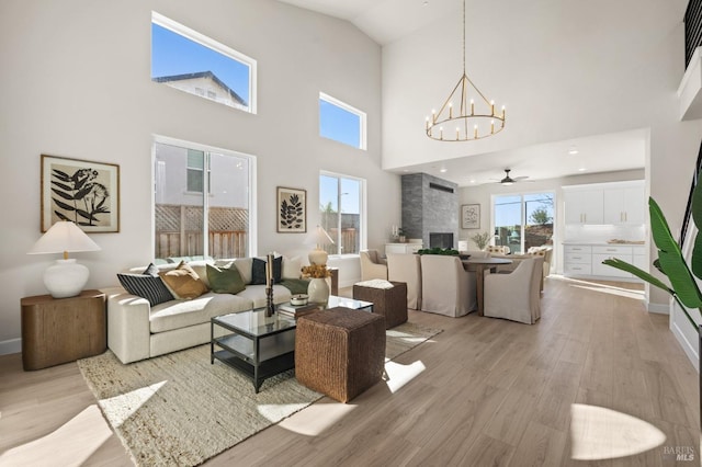 living room with a towering ceiling, a fireplace, ceiling fan with notable chandelier, and light wood-type flooring