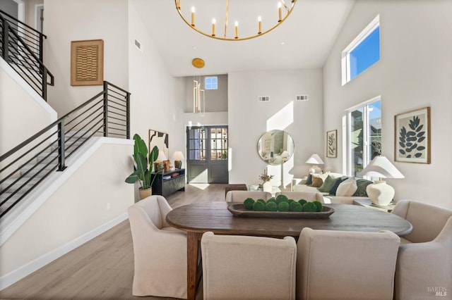 dining room with plenty of natural light, a towering ceiling, an inviting chandelier, and light hardwood / wood-style floors