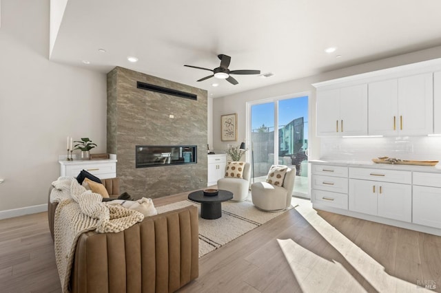 living room featuring ceiling fan, a fireplace, and light hardwood / wood-style flooring