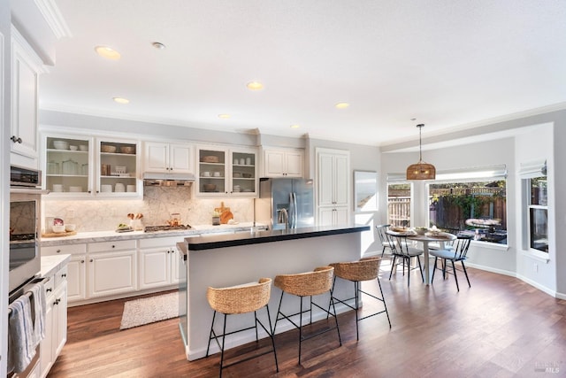 kitchen featuring crown molding, hanging light fixtures, a kitchen island, stainless steel appliances, and white cabinets