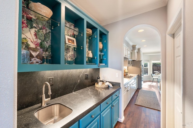 bar with sink, dark wood-type flooring, blue cabinetry, ornamental molding, and decorative backsplash