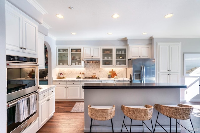 kitchen featuring crown molding, a breakfast bar area, white cabinetry, stainless steel appliances, and an island with sink