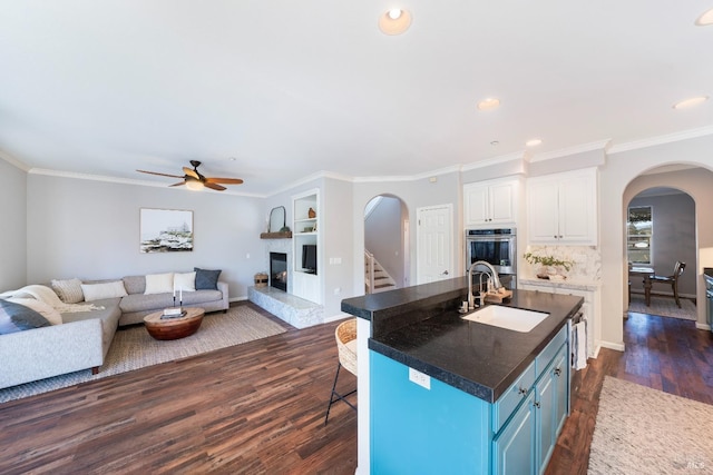 kitchen featuring white cabinetry, an island with sink, sink, blue cabinetry, and stainless steel double oven