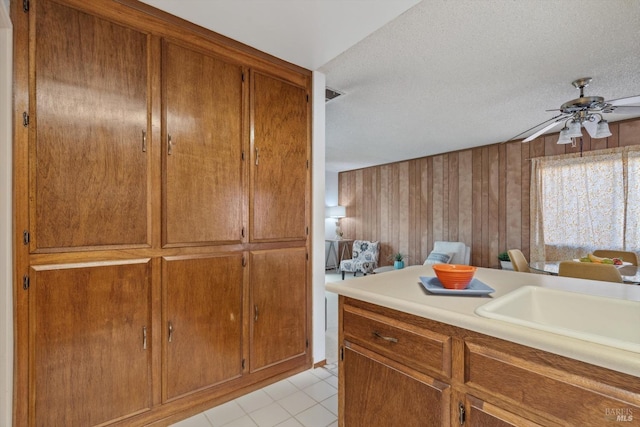 kitchen with ceiling fan, sink, wood walls, a textured ceiling, and light tile patterned floors