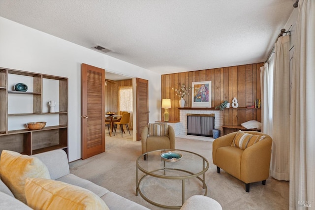 living room with wooden walls, a fireplace, light colored carpet, and a textured ceiling