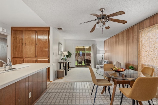 carpeted dining room with ceiling fan, wood walls, sink, and a textured ceiling