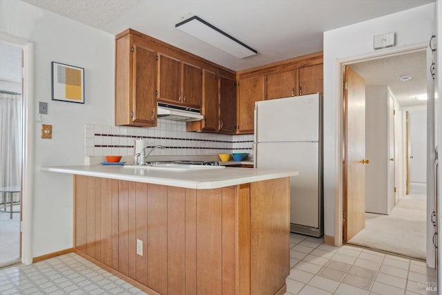 kitchen with backsplash, kitchen peninsula, white fridge, and light tile patterned floors