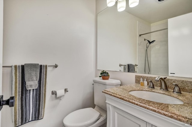 bathroom featuring toilet, tiled shower, and vanity