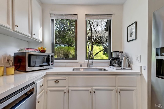 kitchen with light stone countertops, stainless steel appliances, white cabinets, and sink