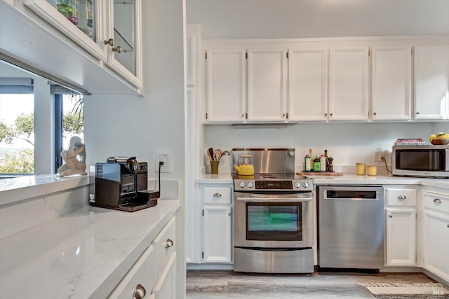 kitchen featuring light wood-type flooring, appliances with stainless steel finishes, white cabinets, and light stone countertops