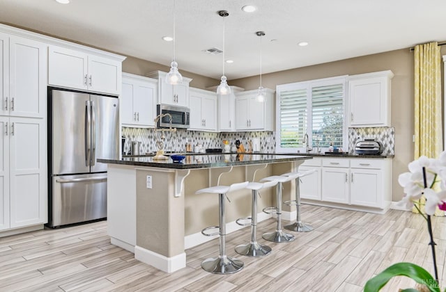 kitchen with appliances with stainless steel finishes, pendant lighting, a center island, light hardwood / wood-style floors, and white cabinetry