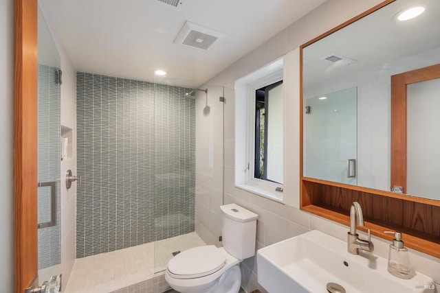 bathroom with sink, a shower with shower door, tile walls, and toilet