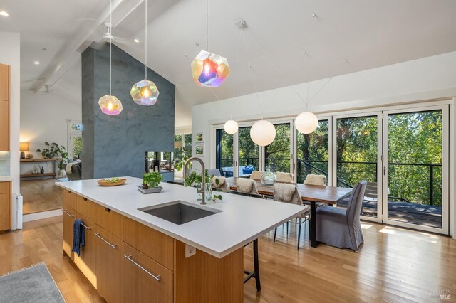 kitchen with a kitchen breakfast bar, a kitchen island with sink, sink, pendant lighting, and lofted ceiling with beams