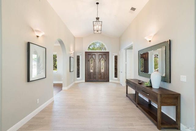 foyer entrance with high vaulted ceiling, light hardwood / wood-style flooring, and an inviting chandelier