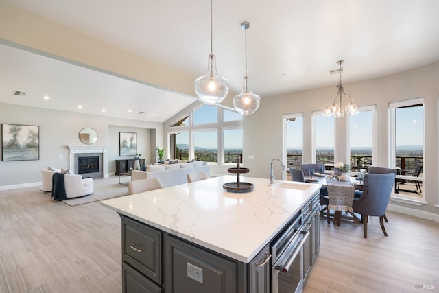 kitchen featuring pendant lighting, a kitchen island with sink, sink, vaulted ceiling, and light stone counters