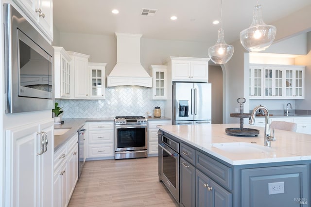 kitchen featuring light stone countertops, appliances with stainless steel finishes, white cabinetry, and custom range hood