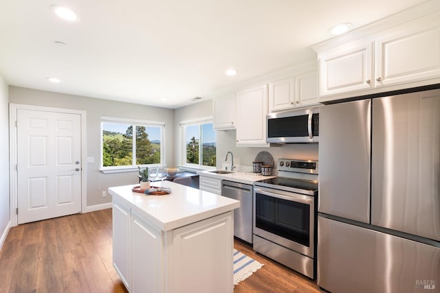 kitchen featuring stainless steel appliances, sink, white cabinets, light hardwood / wood-style floors, and a kitchen island