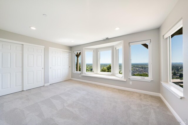 unfurnished bedroom featuring light colored carpet, multiple windows, and multiple closets