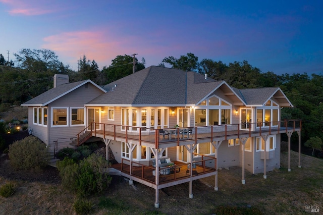 back house at dusk with a sunroom and a wooden deck