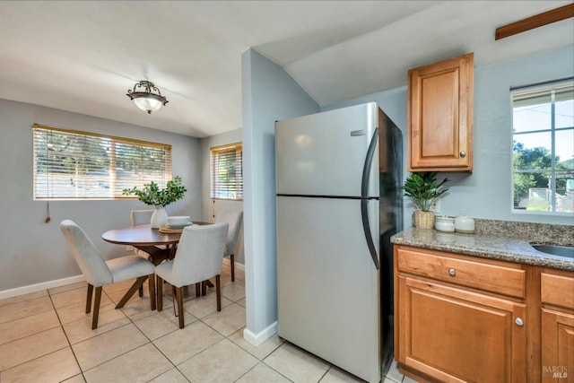 kitchen with sink, stainless steel refrigerator, a wealth of natural light, and light tile patterned flooring