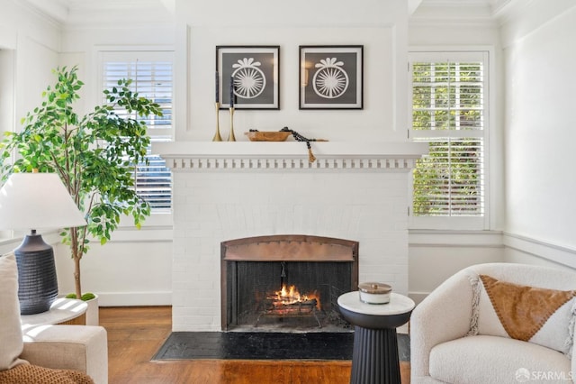 living area with hardwood / wood-style flooring, a brick fireplace, ornamental molding, and plenty of natural light