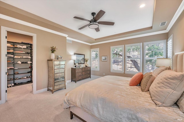 carpeted bedroom with ceiling fan, a walk in closet, a closet, and a raised ceiling