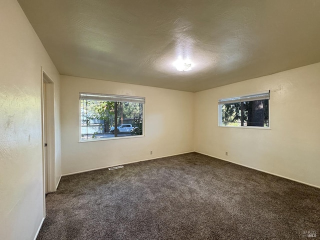 spare room featuring dark carpet and a textured ceiling